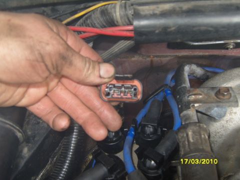 1989 Ford Bronco - Close-up of a hand holding an electrical connector in an engine bay, with spark plug wires visible.