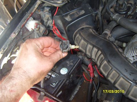 1989 Ford Bronco - Close-up of a hand holding an electrical connector in a vehicle's engine bay.