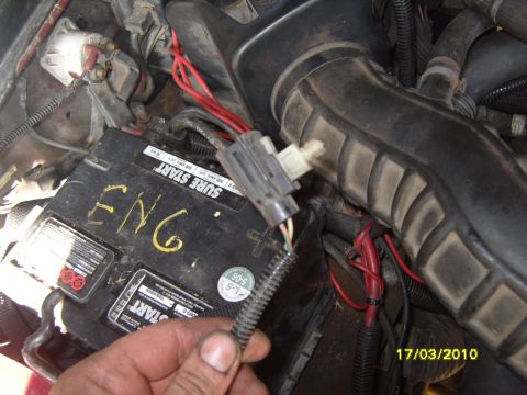 1989 Ford Bronco - A hand disconnects a wire harness near the battery in a vehicle's engine bay.
