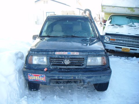 1993 Suzuki Sidekick - A dark blue 1993 Suzuki Sidekick is parked in the snow, a snorkel and various stickers on its front.