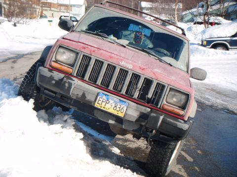 1998 Jeep Cherokee - Red Jeep Cherokee stuck in snow with another vehicle covered in snow in the background.