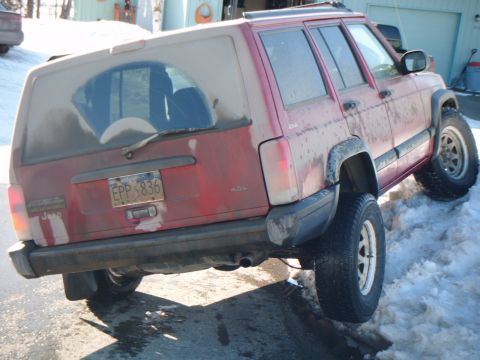 1998 Jeep Cherokee - A red Jeep Cherokee is parked on a snowy surface, showing its rear end and license plate.