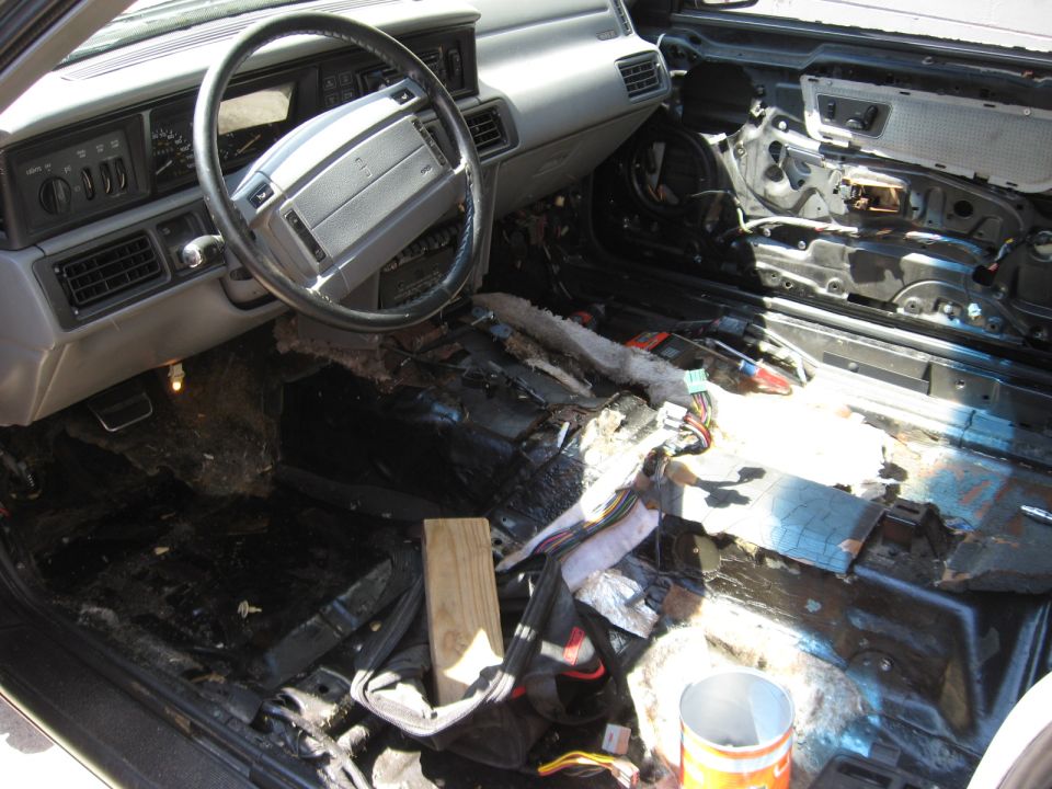 Gutted car interior with carpet and seats removed exposing bare floor pan and wiring
