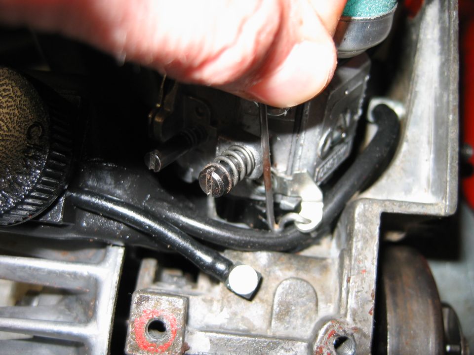 Close-up of carburetor linkage with a finger adjusting a spring