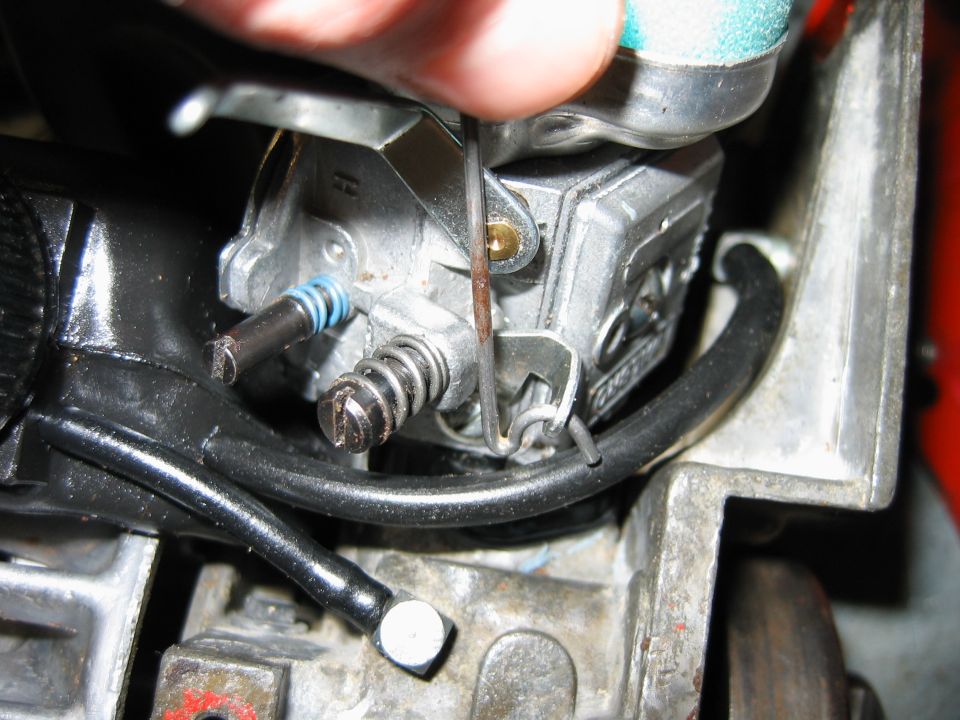 Close-up of a chainsaw carburetor linkage being adjusted