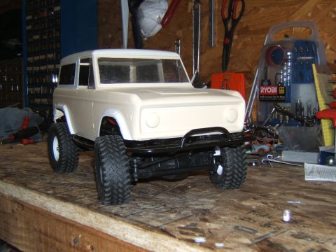 1988 Ford Bronco - This RC crawler model resembles a classic SUV, possibly a Ford Bronco, displayed on a wooden workbench with tools in the background.