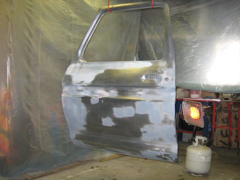 1977 Ford F-150 - A truck door, prepped for paint, is suspended in a workshop with a propane heater in the background.