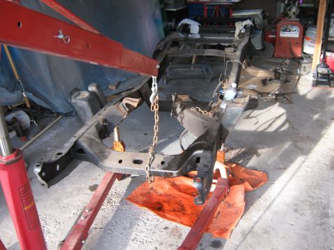 1977 Ford F-150 - The frame of a vehicle is being worked on, supported by an engine hoist and jack stands.