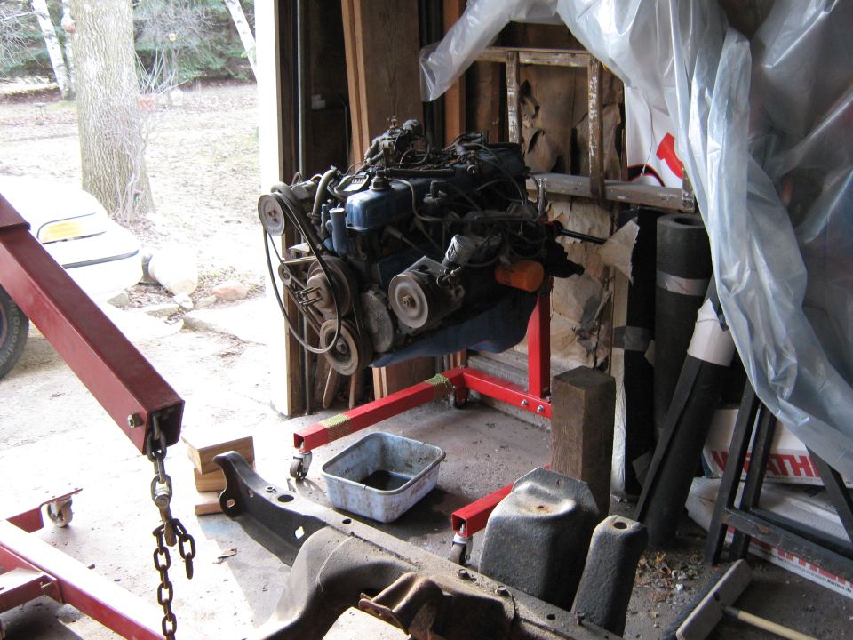 Engine on a red stand in a garage, with a vehicle frame in the foreground