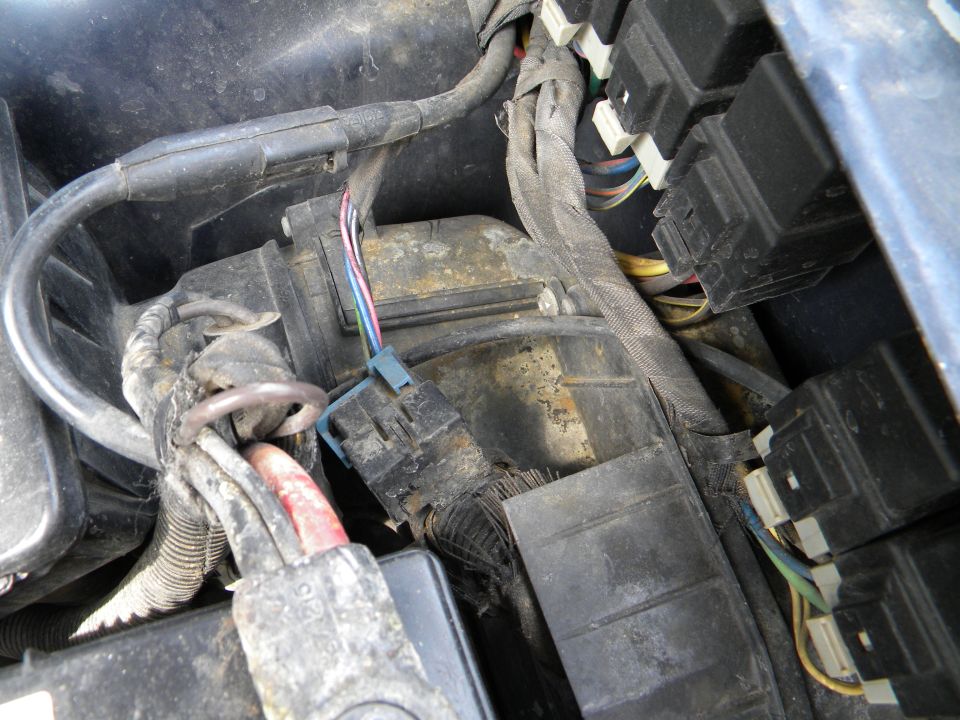 Close-up of engine compartment wiring and fuse box with visible corrosion and frayed wires
