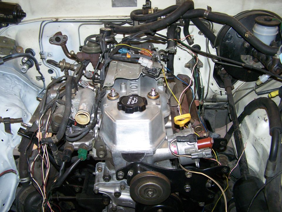 Engine bay with Toyota engine, hoses, and wiring. Visible text: TOYOTA, 22R-E, SUPERMOTORS.NET