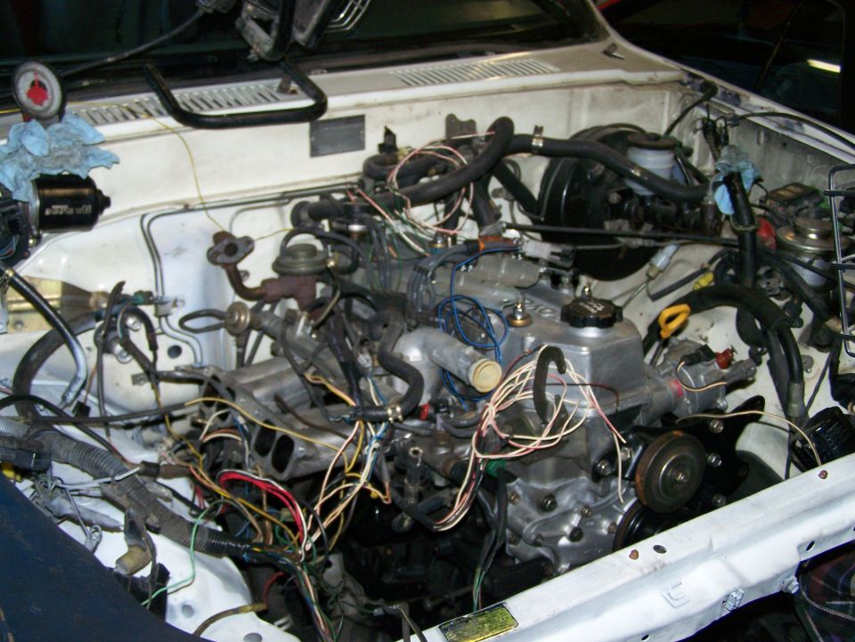 Engine bay with many wires and hoses connected to the engine. A pressure gauge is visible on the left