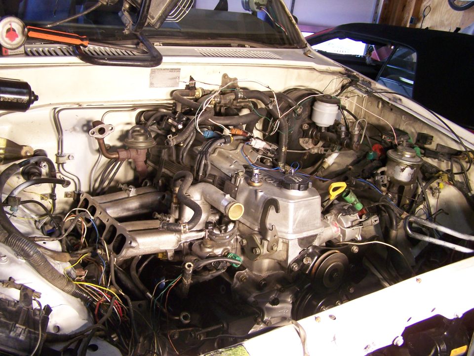 White vehicle engine bay with complex wiring and engine components visible