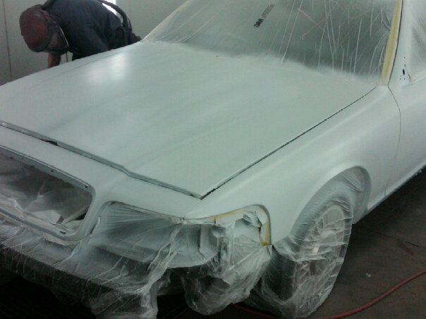 Car body in a paint booth coated in gray primer with masking plastic