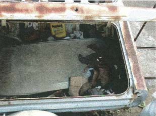 1967 Mercury Cyclone - The trunk interior of a vehicle, containing a yellow bottle and other items, with visible rust on the edges.