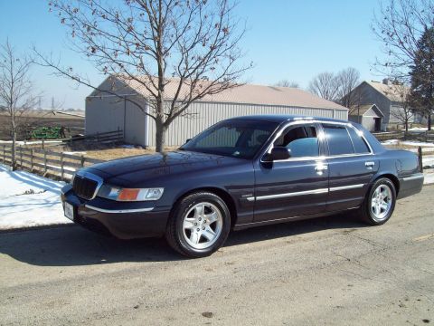1999 Mercury Grand Marquis - Sedan parked on a dirt road with a barn and trees in the background.