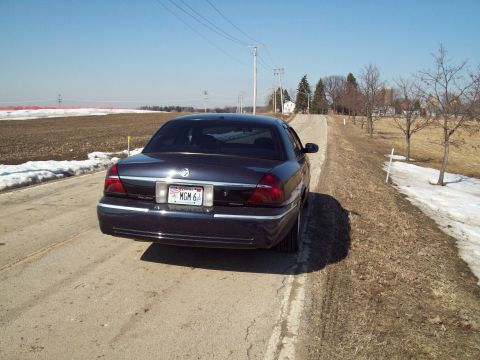 1999 Mercury Grand Marquis - A dark sedan is viewed from the rear on a rural road with snow on the sides.