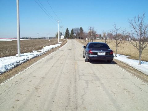 1999 Mercury Grand Marquis - A dark sedan is parked on the shoulder of a country road with snow still visible on the ground.