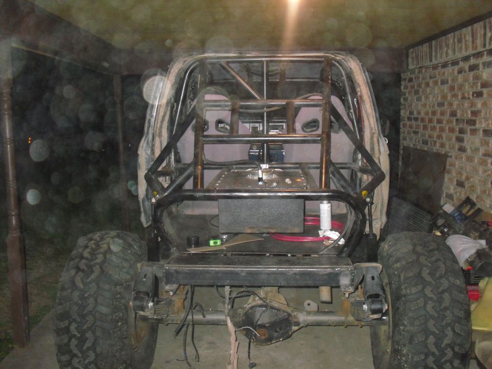 Rear view of a heavily modified off-road vehicle with a prominent roll cage, large tires, and exposed rear axle