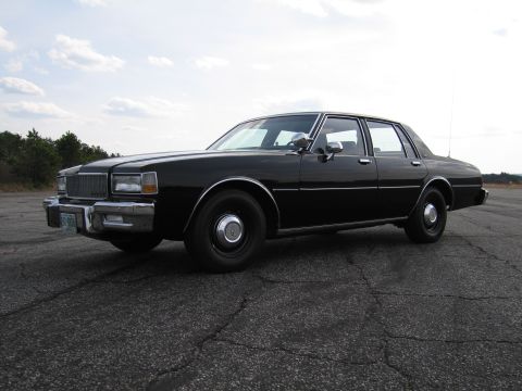 1991 Ford Crown Victoria LTD - This black sedan, likely from the early 1980s, is viewed from the front three-quarter angle on a paved surface.