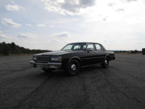 1991 Ford Crown Victoria LTD - This black sedan is parked on an asphalt lot under a cloudy sky.