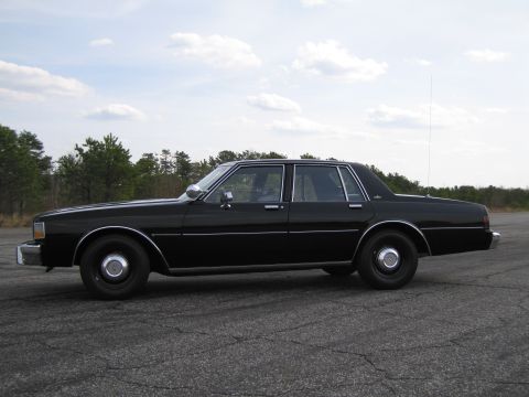 1991 Ford Crown Victoria LTD - Side profile of a black sedan parked outdoors on a cracked asphalt surface under a cloudy sky.
