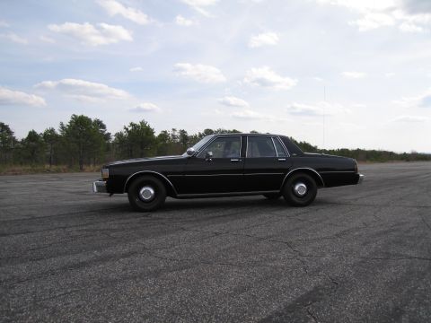 1991 Ford LTD Crown Victoria - This black sedan is parked on an asphalt surface with trees and a cloudy sky visible.