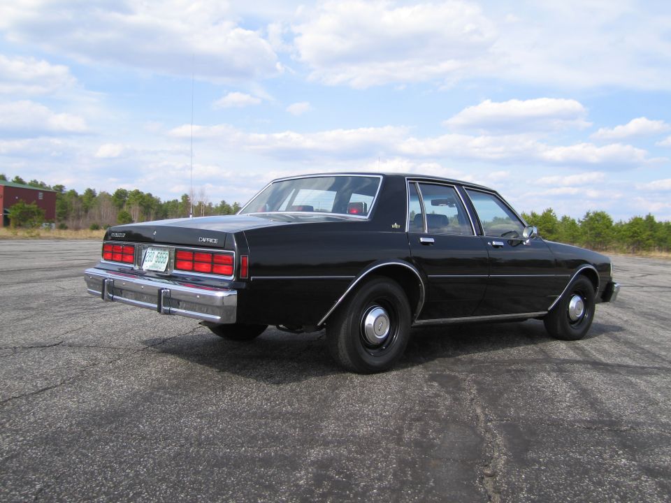 Black sedan parked on asphalt lot. Rear view shows taillights and chrome bumper