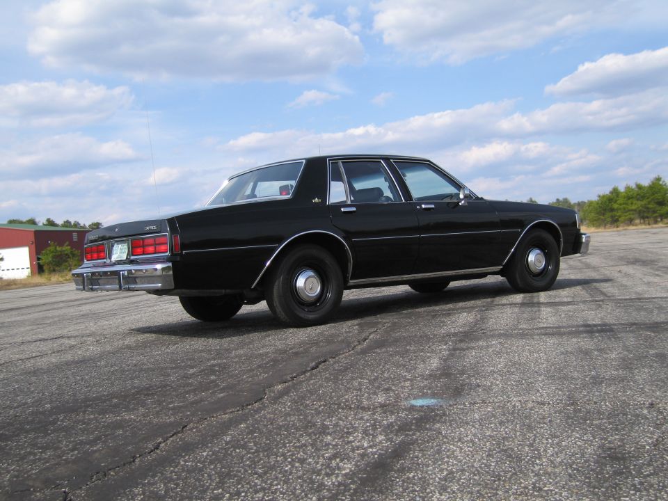 Black sedan parked on asphalt, rear-left quarter view. Chrome trim, steel wheels
