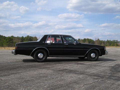 1991 Ford LTD Crown Victoria - Side profile of a black sedan parked on asphalt under a cloudy sky.