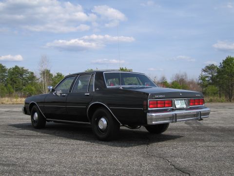 1991 Ford LTD Crown Victoria - This black sedan, likely from the 1980s, is viewed from the rear with a clear license plate and Chevrolet badging visible.