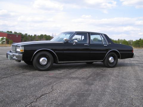 1991 Ford LTD Crown Victoria - Side profile of a black sedan parked outdoors on a cracked asphalt surface under a cloudy sky.