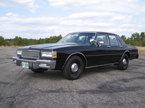 1991 Ford LTD Crown Victoria - This black sedan has a prominent chrome grille and a license plate with readable text.