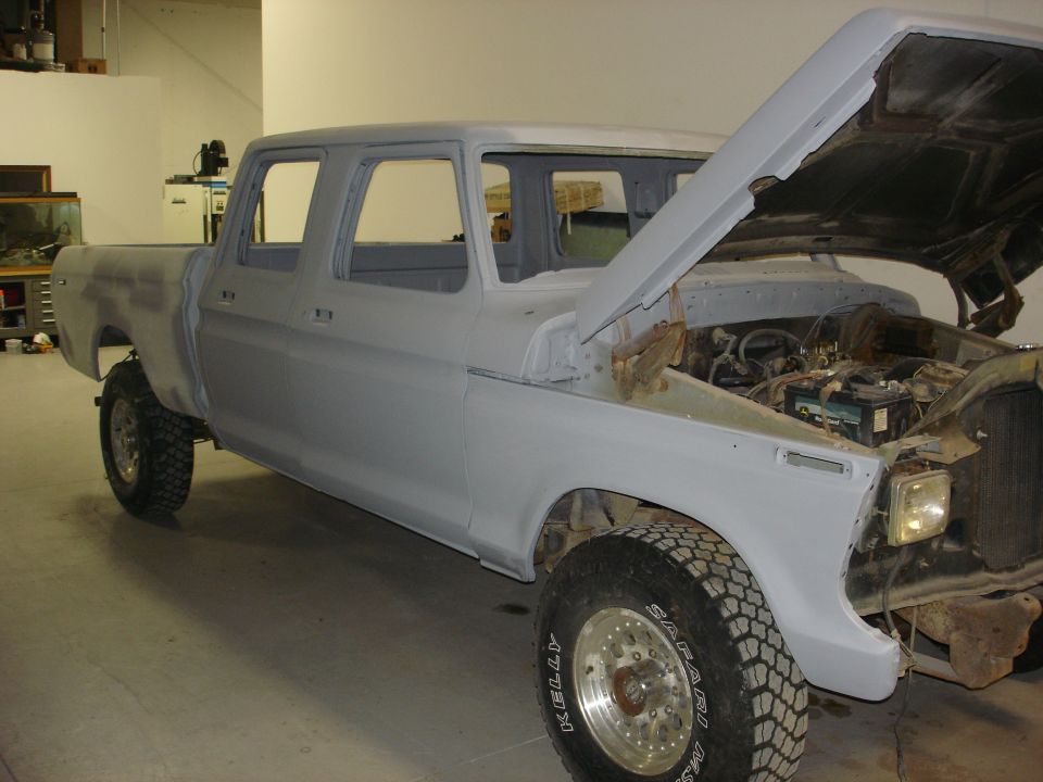 Gray crew cab pickup truck, hood open, undergoing bodywork, 3/4 front view