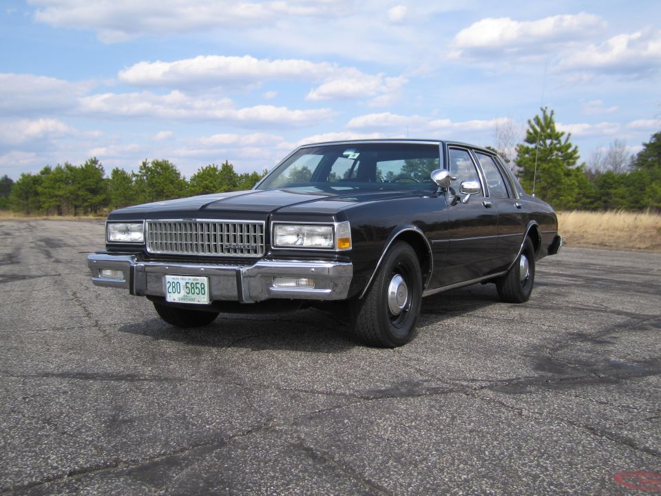 Black sedan parked on asphalt lot, trees and cloudy sky in background. License plate reads 280 5858
