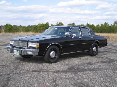 1991 Ford LTD Crown Victoria - This black sedan, likely from the early 1980s, is viewed from the front three-quarter angle on a paved surface.