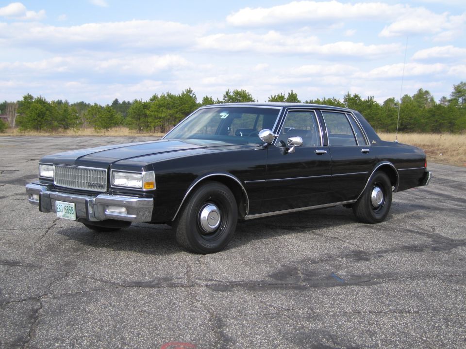 Black sedan parked on cracked asphalt, front 3/4 view. Chrome grille, bumpers, and trim. License plate reads '380 5958'