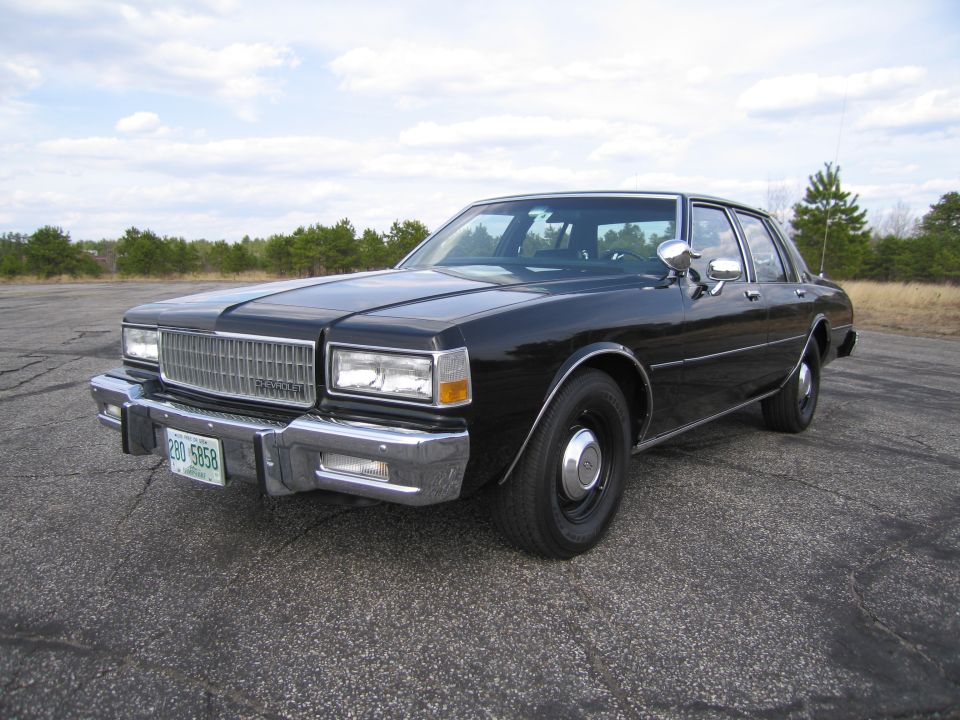 Black sedan parked on asphalt lot, trees in background. License plate reads 280 5858