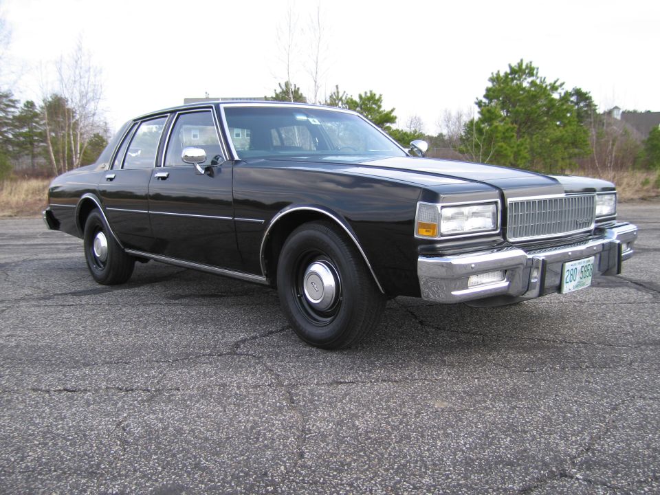 Black 1980s sedan with chrome grille and bumper, parked on cracked asphalt