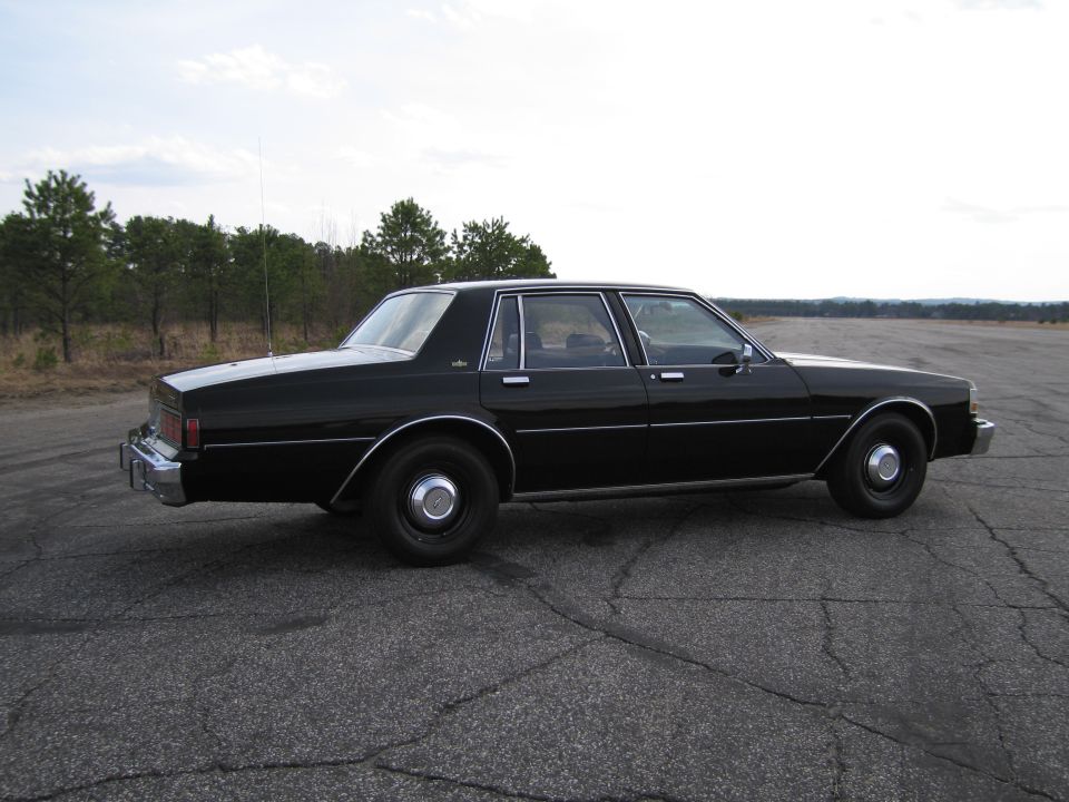 black sedan parked on asphalt, trees in background