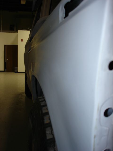 1979 Ford F-250 - Side view of a white pickup truck with a primer finish, showing tire tread and a doorway in the background.