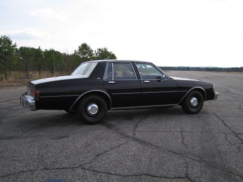 1991 Ford LTD Crown Victoria - This black sedan, likely from the early 1980s, is seen from the side on a cracked asphalt surface.