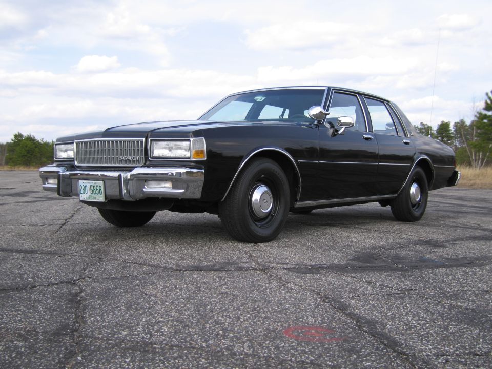 Black sedan parked on asphalt, front 3/4 view. Chrome grille, headlights, and bumpers. License plate visible