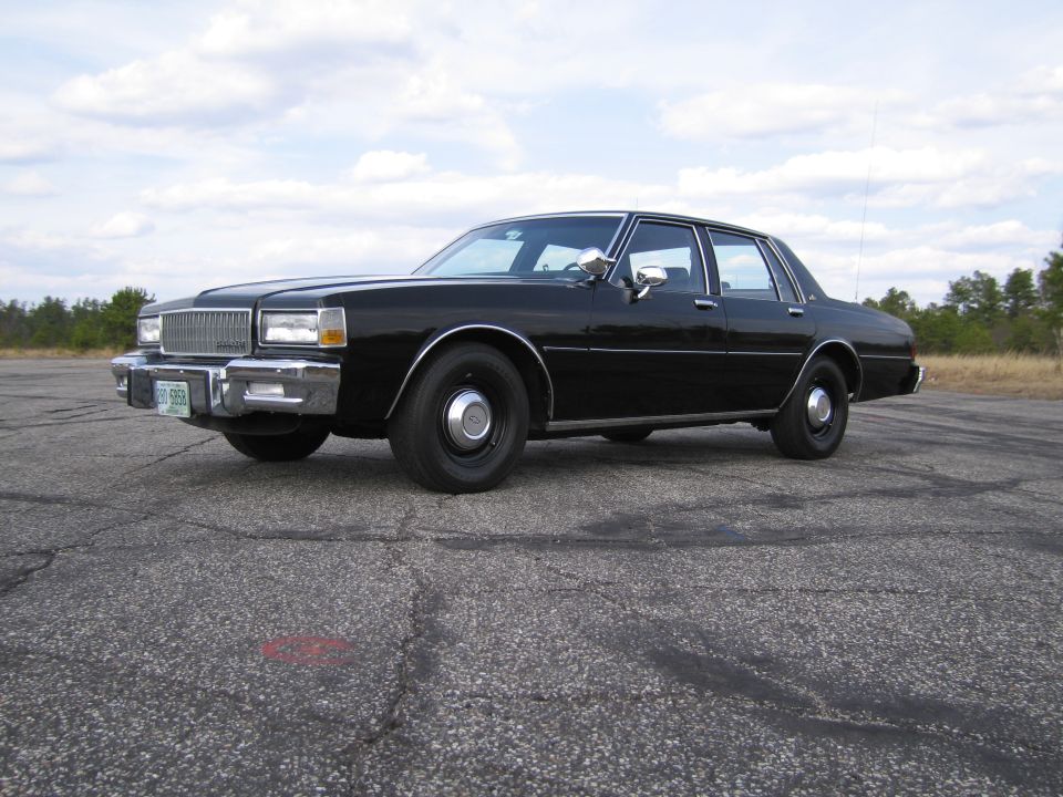 Black sedan parked on asphalt lot, front quarter view. Appears to be a late 1970s or early 1980s model