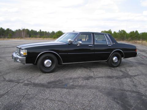 1991 Ford LTD Crown Victoria - A black sedan is parked outdoors on a paved surface with trees visible in the distance.