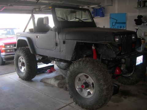 1991 Jeep Wrangler - A black Jeep Wrangler with off-road tires and suspension modifications is parked in a garage next to a red pickup truck.