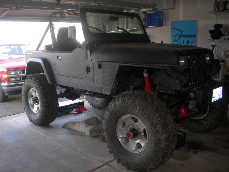 Black Jeep Wrangler with large tires and red shocks, parked next to a red pickup truck