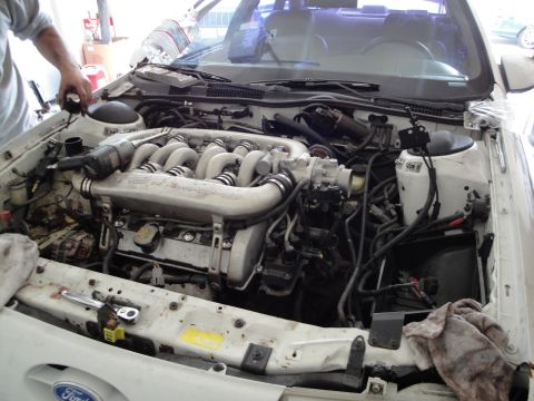 1989 Ford Taurus - The engine bay of a car is shown with the V6 engine exposed, detailing the complex network of hoses and wires.
