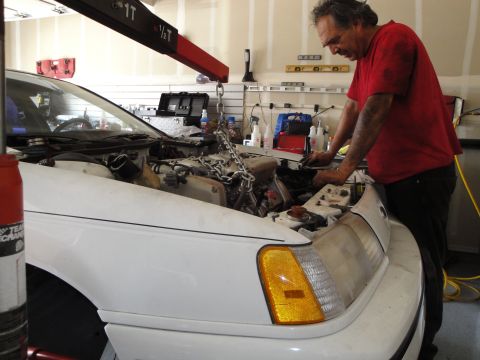 1989 Ford Taurus - A man works on the engine of a white 1989 Ford Taurus in a garage.