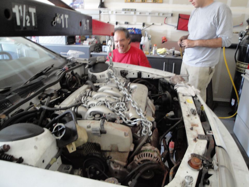 Engine being lifted from white car with engine hoist; garage setting